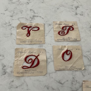 May include: Four vintage Plumetis-Express No. 3 iron-on patches featuring red embroidered cursive letters P, T, D, and O. Each letter is centered on a square off-white paper backing with printed text including Made in France and patent details.