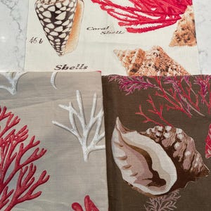 May include: Fabric panels with seashell and coral designs. The panels display seashells and coral in brown, red, and white. One panel has the word "Shells" printed on it. The designs are suitable for home decor.