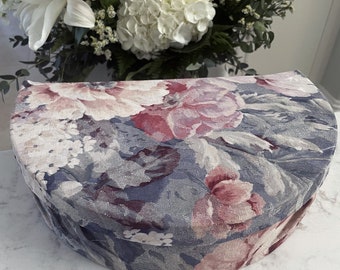 May include: A round, floral patterned storage box with a blue background and pink and white flowers. The box is made of fabric and has a soft, quilted texture.