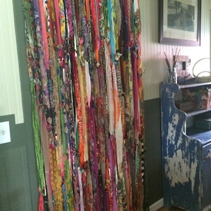 May include: A colorful fabric curtain made of strips of fabric in various colors and patterns. The curtain is hanging from a rod and is in front of a wall.