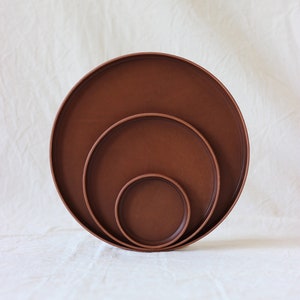 Op de afbeelding: Drie ronde, bruine schalen in verschillende maten, op elkaar gestapeld.