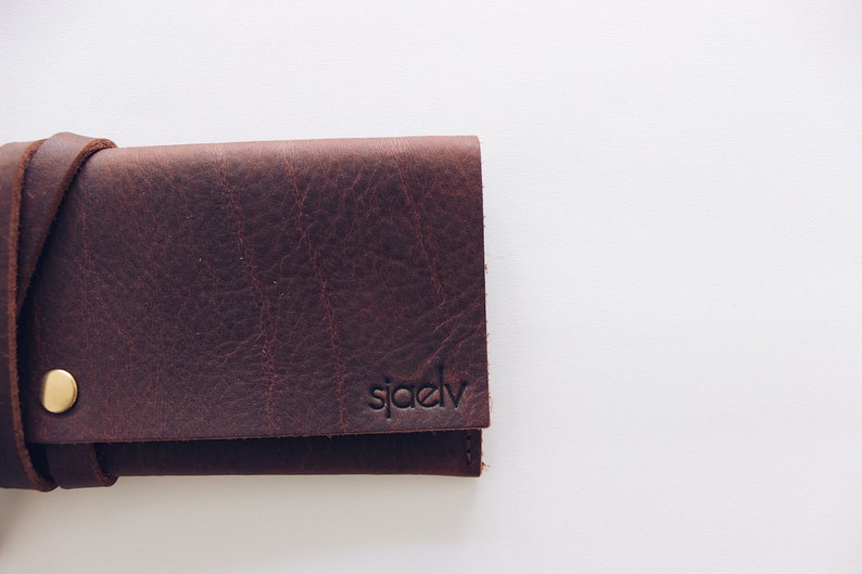 May include: A brown leather wallet with a brass button and the word "sj&aelig;dv" embossed on the front.