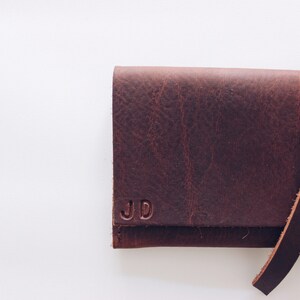 May include: A brown leather wallet with a strap closure and the initials "JD" embossed on the front.