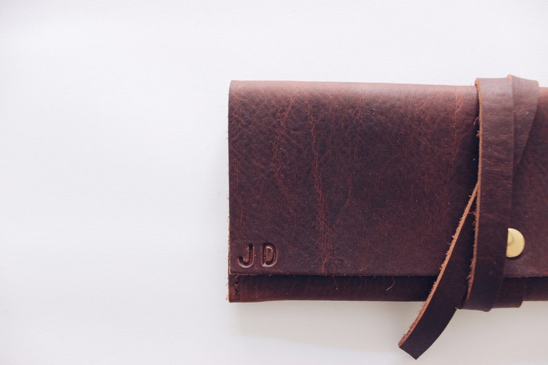 May include: A brown leather wallet with a strap closure and the initials "JD" embossed on the front.