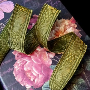 May include: Gold metallic ribbon with a woven design. The ribbon has a detailed pattern and is slightly curled. The ribbon is on a background with a floral design and a butterfly.