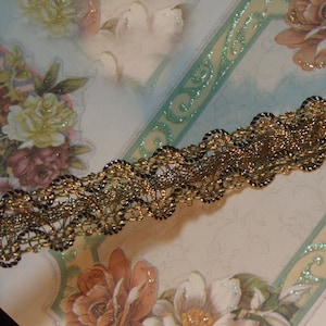 May include: Gold and black lace trim with a delicate, intricate design. The trim has a wavy, scalloped edge.