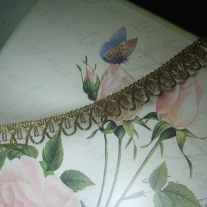 May include: Gold trim with a scalloped edge. The trim is on a white background with a floral design.