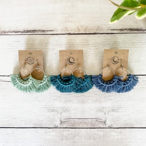 May include: Three pairs of handmade macrame earrings with silver hoops. The earrings are in shades of teal, blue, and green.