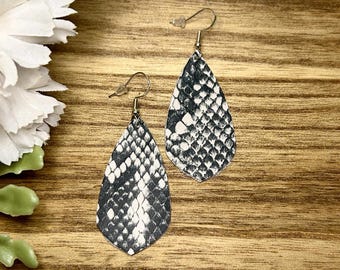 May include: A pair of dangle earrings with a teardrop shape. The earrings are made of black and white faux snakeskin leather.