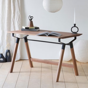 May include: A wooden desk with black metal supports and legs. A white paper lantern hangs above the desk. The desk has books, scissors, and a candle holder with a white candle. The desk is 55 inches long.