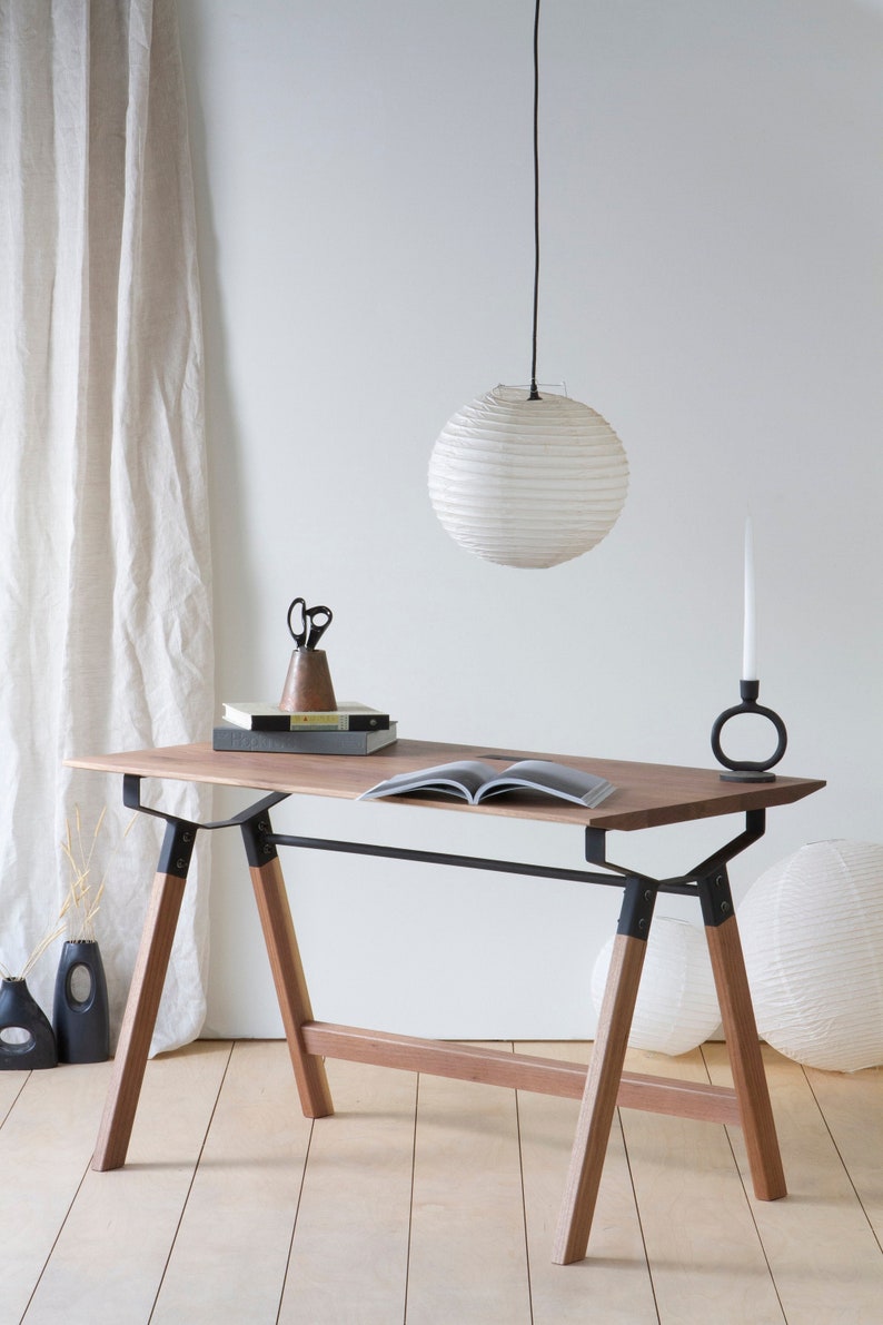 May include: A wooden desk with black metal supports and legs. A white paper lantern hangs above the desk. The desk has books, scissors, and a candle holder with a white candle. The desk is 55 inches long.