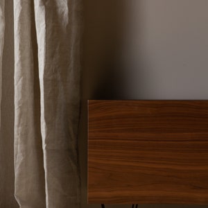 May include: A wooden cabinet with a dark brown finish and black hairpin legs. The cabinet is positioned in front of a light beige wall and a sheer linen curtain.