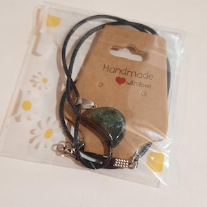 May include: A green stone pendant necklace with a black cord and silver-tone clasp. The necklace is packaged in a clear plastic bag with a brown tag that reads "Handmade with love."