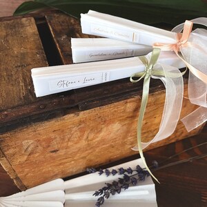 Puede incluir: Tres abanicos de papel blanco con letras doradas atados con una cinta blanca y cintas de color verde y melocot&oacute;n. Los abanicos est&aacute;n etiquetados con "Stefano e Laura", "Giuseppina e Davide" y "Andrea e Camilla".