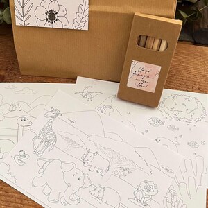 May include: A brown paper gift bag with a floral tag that reads "Clarissa - 26.09.2026 - Giacomo." Several black and white coloring pages with animal illustrations are in front of the bag, along with a small box of colored pencils.