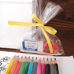 May include: A set of colored pencils, a pencil sharpener, and a small eraser in a clear plastic bag tied with a yellow ribbon. The pencils are arranged in a row, with the eraser and sharpener in the background. The text on the eraser reads "LYRA, OROM-TECHNICO, PVC FREE, ART. NR. 713300".