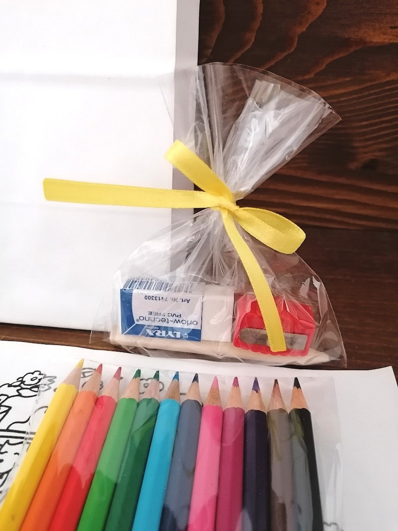 May include: A set of colored pencils, a pencil sharpener, and a small eraser in a clear plastic bag tied with a yellow ribbon. The pencils are arranged in a row, with the eraser and sharpener in the background. The text on the eraser reads "LYRA, OROM-TECHNICO, PVC FREE, ART. NR. 713300".