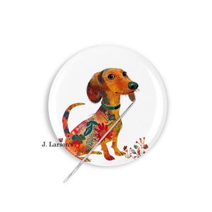 May include: A white, round decorative plate featuring a watercolor illustration of a dachshund dog with floral patterns. The dog is orange and brown with a green nose and collar. The text "J. Larson's" is printed on the plate.