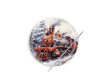 Può includere: Un bottone rotondo bianco con un'illustrazione ad acquerello di un treno a vapore rosso e nero d'epoca in una foresta innevata. Un ago d'argento è posto diagonalmente sul bottone.