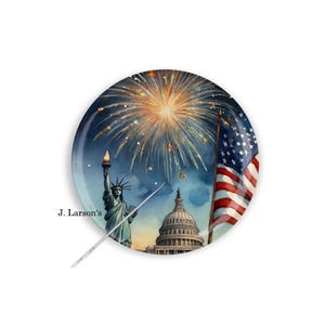 May include: Round decorative plate featuring a watercolor illustration of fireworks, the Statue of Liberty, the U.S. Capitol, and the American flag. The plate has a dark blue background with the text "J. Larson's".