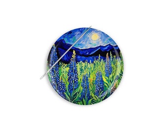 Può includere: Un bottone rotondo con un dipinto di un campo di fiori di lupino blu con una catena montuosa sullo sfondo. Il cielo è blu scuro con un sole giallo brillante.