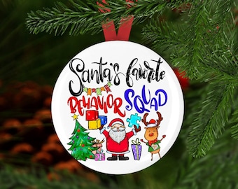Può includere: Addobbo natalizio rotondo bianco con il testo "La squadra di comportamento preferita di Babbo Natale" in lettere colorate. L'addobbo presenta un Babbo Natale dei cartoni animati, una renna, un albero di Natale e blocchi di costruzione colorati.