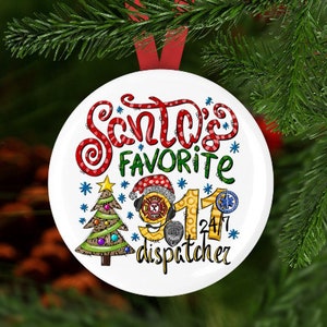 May include: A white Christmas ornament with the text "Santa's Favorite Dispatcher" in red, green, and black. The ornament features a Christmas tree, a firefighter's helmet, and the numbers "911" and "24/7". The ornament is hanging from a red ribbon.