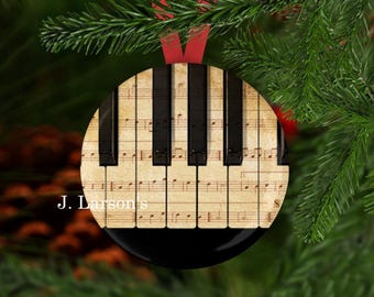 May include: A round Christmas ornament with a black background and a vintage image of a piano keyboard with sheet music. The ornament is decorated with a red ribbon.