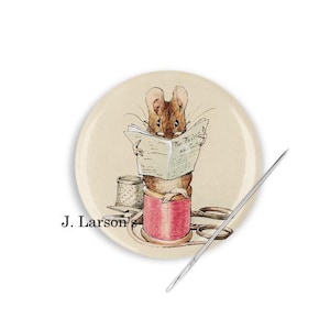 May include: A round button featuring a cartoon mouse sitting on a spool of thread, reading a newspaper titled "The Tailor and Cutter".