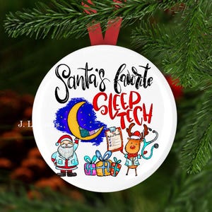 May include: White round Christmas ornament with a cartoon illustration of Santa Claus and a reindeer. The ornament has the text "Santa's favorite sleep tech" in black script.