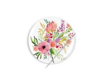 Può includere: Un cuscino per spilli in ceramica bianca con un design floreale ad acquerello con fiori rosa, rossi e gialli. Un ago d'argento è posto sopra il cuscino per spilli.