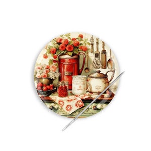 May include: A round ceramic plate with a vintage kitchen scene. The plate features a red pitcher with flowers, a teapot, a cup, jars of jam, and a bowl of strawberries. The plate has a white background with a brown border.