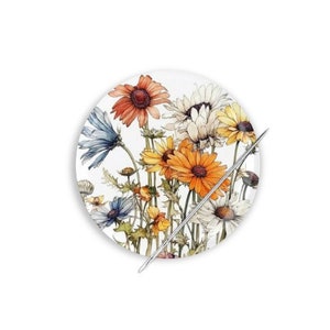 May include: A round needle minder with a white background and a colorful floral design. The flowers are in shades of orange, yellow, blue, and white. A silver needle is placed on top of the needle minder.