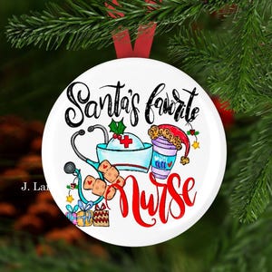 K&ouml;nnte beinhalten: Ein wei&szlig;er Weihnachtsschmuck mit dem Text "Santa's Favorite Nurse" in schwarzer und roter Schrift. Der Schmuck zeigt eine Krankenschwesterm&uuml;tze, ein Stethoskop, eine Kaffeetasse und Pflaster. Er h&auml;ngt an einem roten Band vor gr&uuml;nen Tannennadeln.