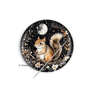 May include: A round, black decorative pin with a watercolor illustration of a squirrel sitting on a branch under a full moon and stars. The pin has a silver needle and the artist's signature, "J. Larson."