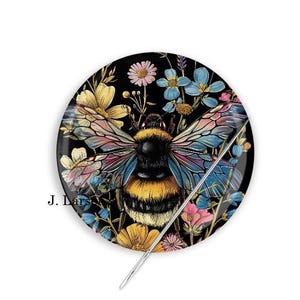 May include: A black and white bee with yellow stripes and iridescent blue and pink wings surrounded by colorful flowers on a black background. The bee is centered in the image and the flowers are arranged around it. A needle is sticking through the bee and the flowers.
