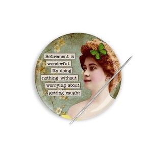 May include: A round pincushion with a vintage-style image of a woman with a green flower in her hair. The pincushion has a quote that reads "Retirement is wonderful. It's doing nothing without worrying about getting caught."