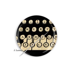 May include: A black round decorative plate featuring a vintage typewriter keyboard design. The keys are beige with black lettering, and the plate has a silver needle-like object. The text "J. Larson's" is visible.