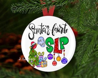Può includere: Ornamento natalizio bianco con la scritta "Santa's favorite SLP". L'ornamento presenta un uccello dei cartoni animati con un cappello da Babbo Natale, un albero di Natale e scatole regalo. Il testo aggiuntivo include "Let's talk!" e termini di logopedia.