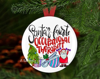 Può includere: Ornamento natalizio bianco con la scritta "Santa's Favorite Occupational Therapist" in nero e rosso. L'ornamento presenta un albero di Natale, Babbo Natale e strumenti terapeutici.