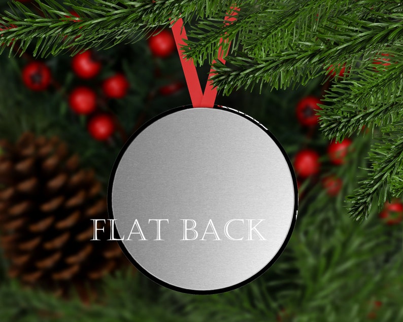 K&ouml;nnte beinhalten: Eine runde, silberfarbene Weihnachtskugel mit schwarzem Rand und rotem Band zum Aufh&auml;ngen. Auf der Kugel steht "FLAT BACK". Der Hintergrund zeigt Tannenzweige, rote Beeren und einen Tannenzapfen.