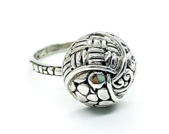 May include: A silver ring with a textured, spherical design. The ring features intricate woven and patterned details.