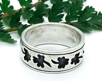 Op de afbeelding: Een zilveren ring met een zwart klaverblad ontwerp. De ring is breed en heeft een glad oppervlak.