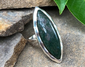 May include: A silver ring with a green moss agate stone set in a hammered silver bezel. The ring is a statement piece with a unique and natural look.