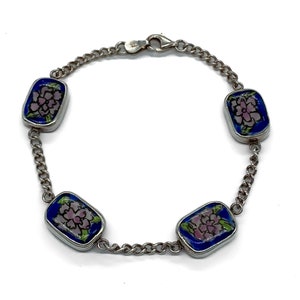 May include: A silver chain bracelet with four rectangular blue and pink enamel charms featuring floral designs.