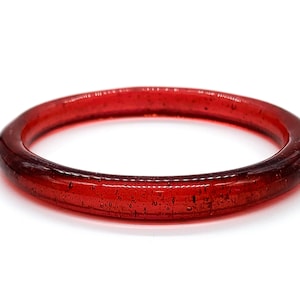 Puede incluir: Un brazalete de vidrio rojo con un acabado moteado.