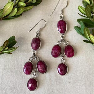 Op de afbeelding: Een paar oorhangers met meerdere ovale robijnstenen. De oorhangers zijn gemaakt van zilver en hebben een eenvoudig ontwerp.