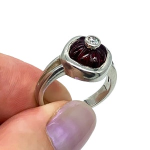 Op de afbeelding: Een zilveren ring met een gegraveerde rode steen en een kleine diamant in het midden.