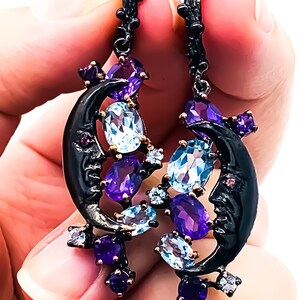 May include: A pair of black oxidised silver earrings with a crescent moon design. The earrings are adorned with amethyst and blue topaz gemstones.