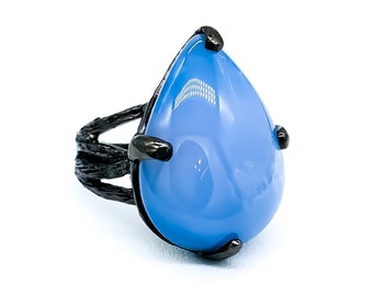 Op de afbeelding: Een zwarte ring met een grote, traanvormige blauwe edelsteen. De ring heeft een unieke, gedraaide band.